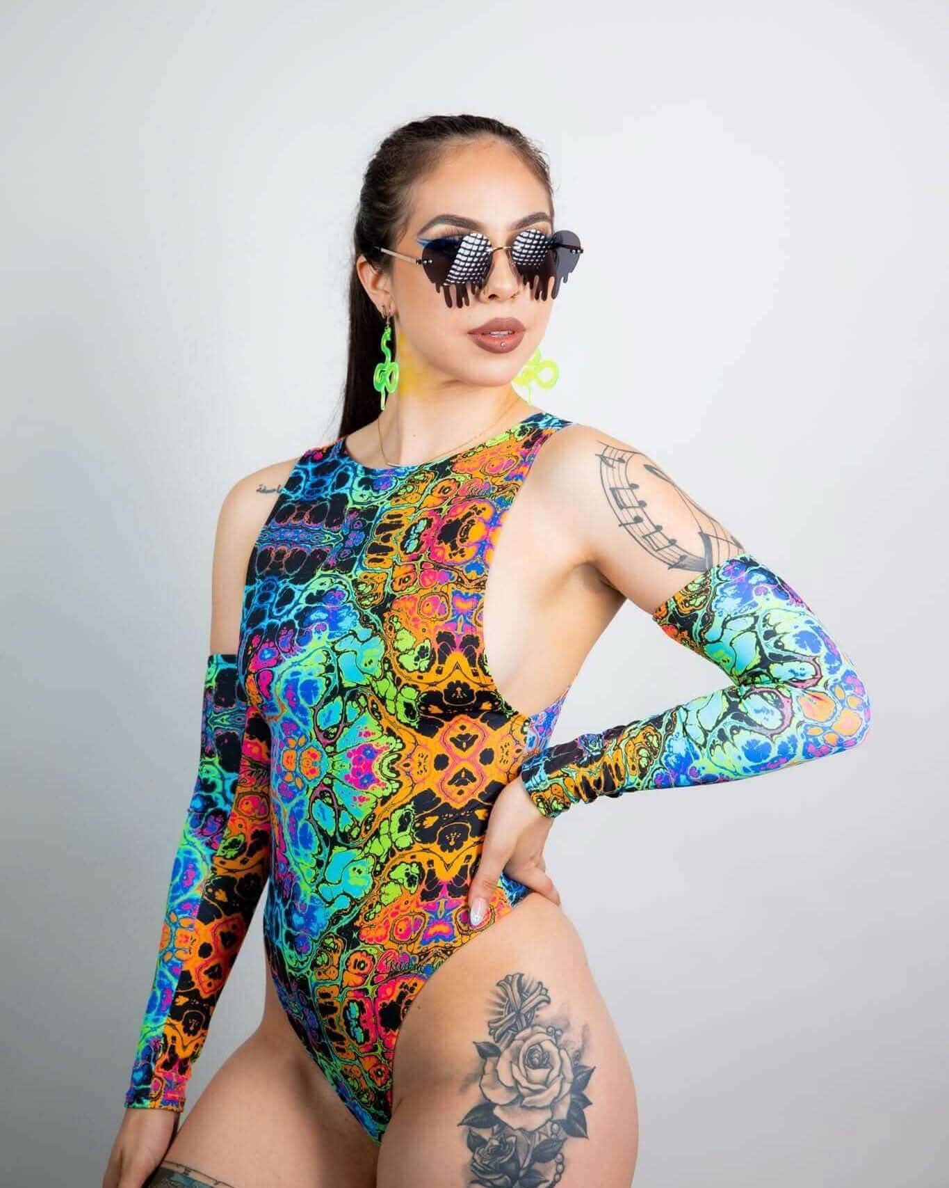 Model wearing Lucidity Sideboob Bodysuit in psychedelic rainbow print, showcasing rave outfits style with sunglasses and accessories.