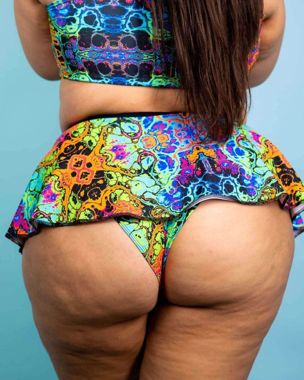 Colorful back view of a model wearing a vibrant Lucidity Swirl Skirt paired with a matching top, ideal for rave outfits.