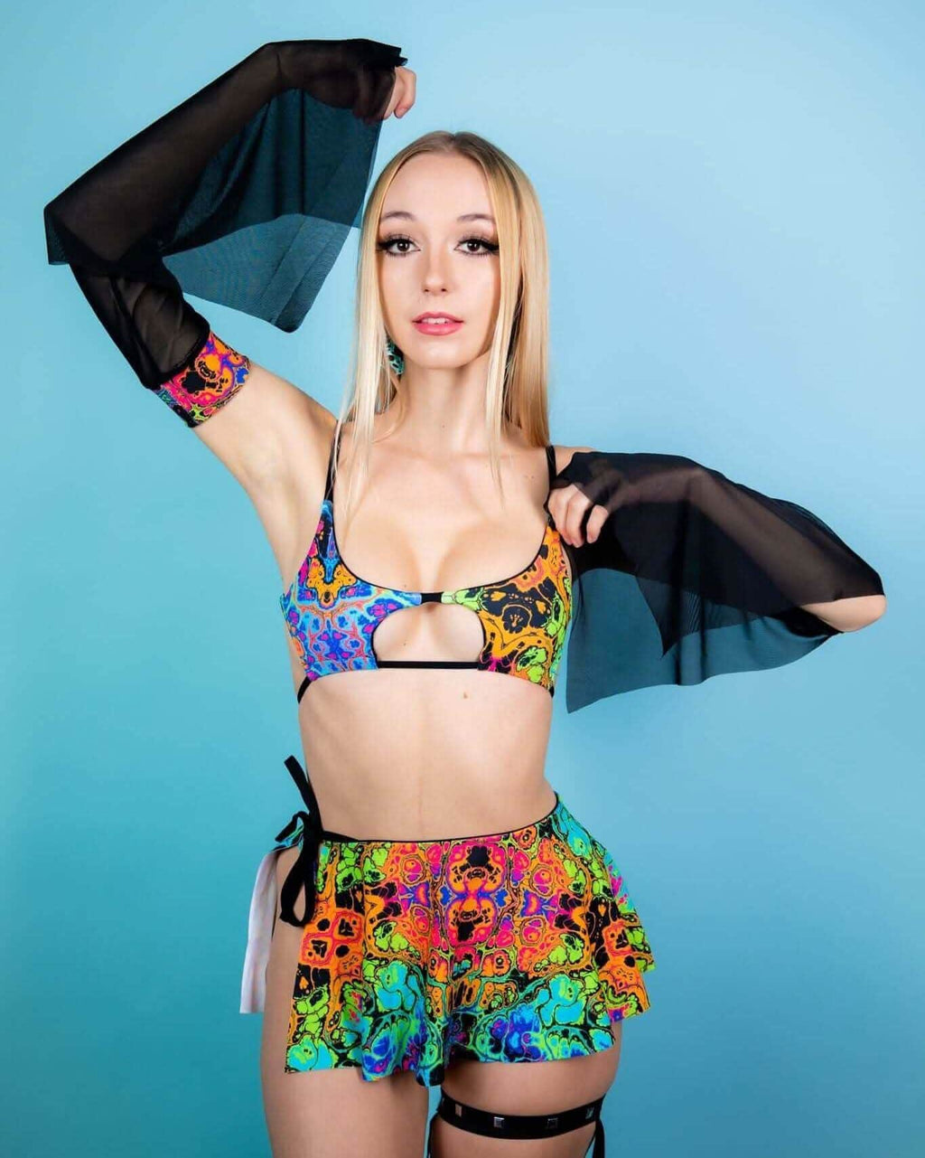 Model wearing a colorful rave outfit featuring a vibrant cropped top and frilled shorts with sheer sleeves.