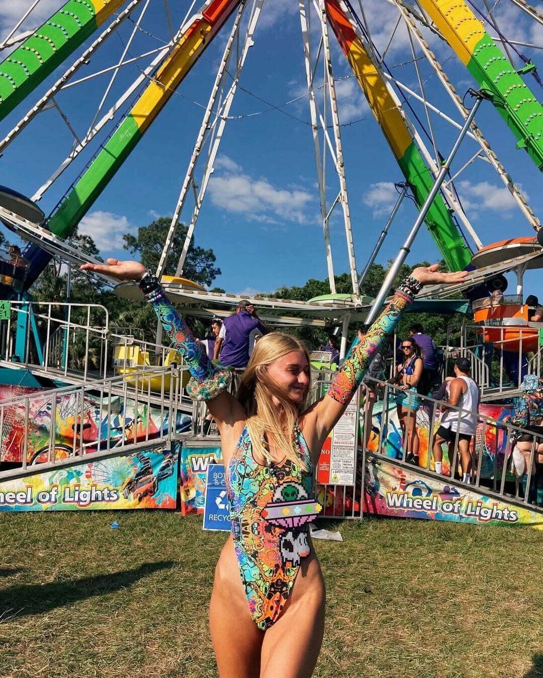 Woman in a psychedelic rainbow one-piece swimsuit celebrating at a vibrant carnival. Perfect for rave outfits and festivals.