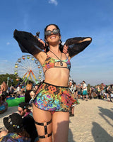 Smiling woman in vibrant psychedelic outfit at a festival, showcasing colorful rave outfit with tie-straps and accessories.