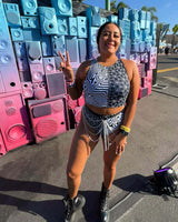 Woman wearing a stylish rave outfit with a unique pattern, posing in front of colorful speaker art backdrop.