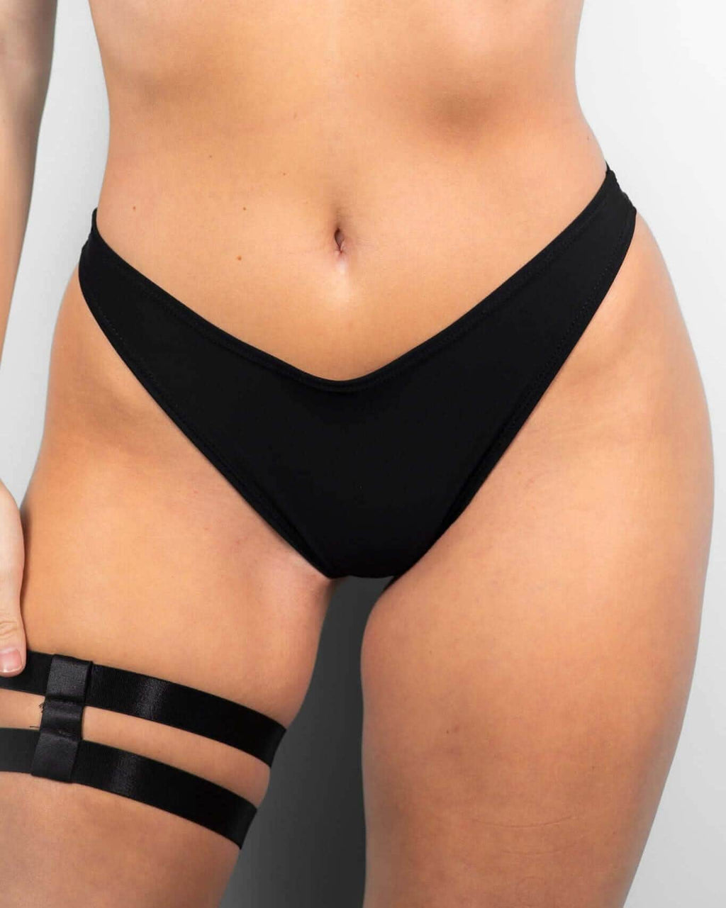 Matte black Brazilian bikini bottoms featuring a low-waisted, cheeky cut, perfect for trendy rave outfits.