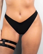Matte black Brazilian bikini bottoms featuring a low-waisted, cheeky cut, perfect for trendy rave outfits.