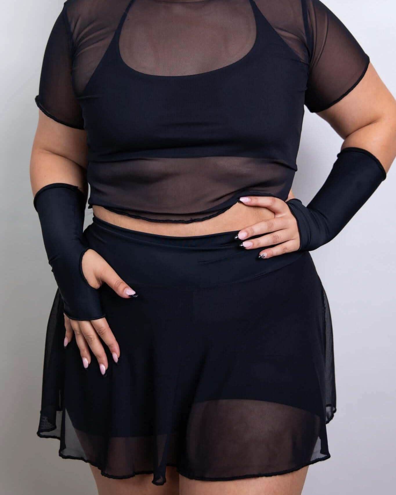 model wearing a black sheer crop top and skirt, paired with coordinating arm sleeves, perfect for rave outfits.