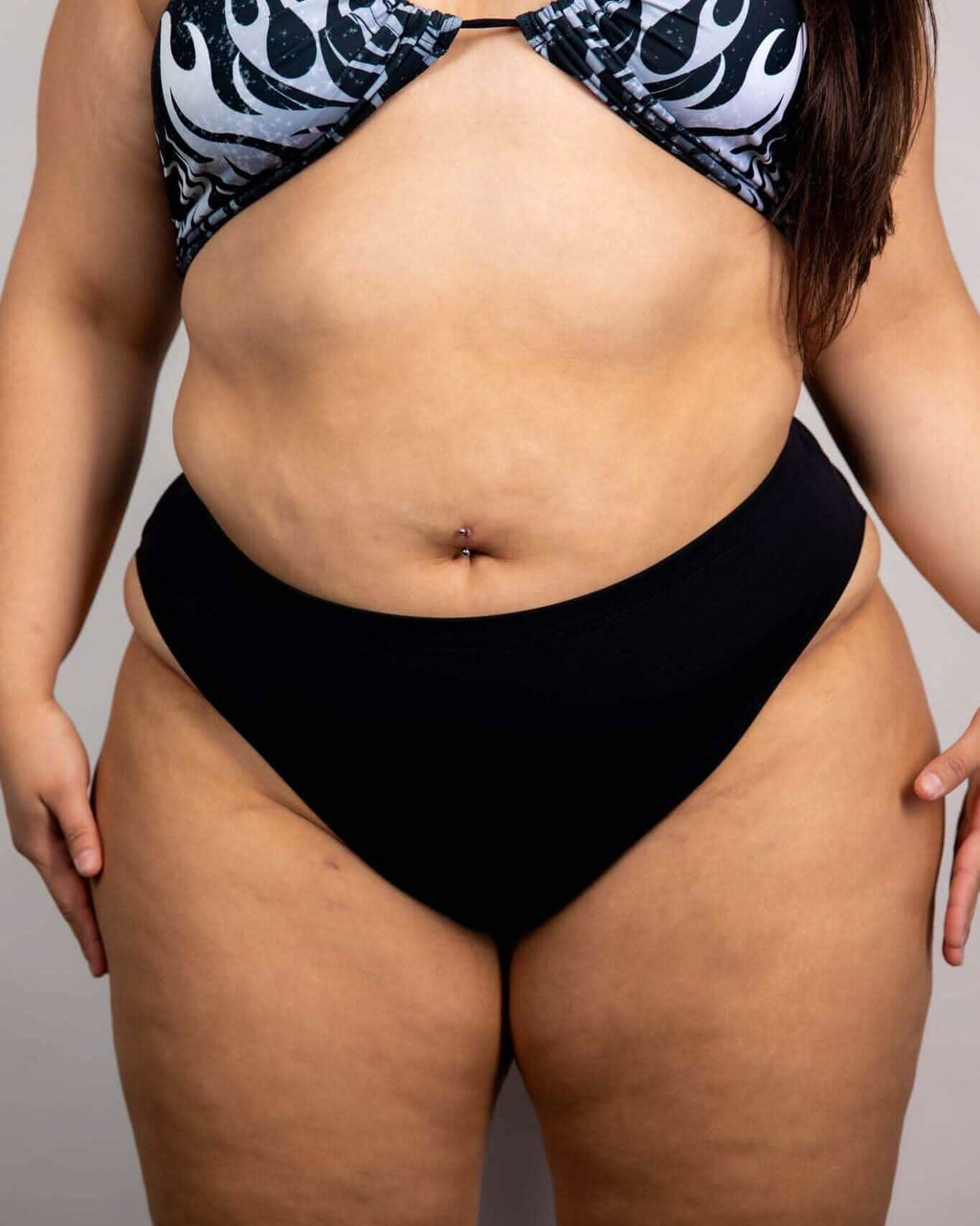 High-waisted black Brazilian bottoms showcased with a colorful flame-patterned bikini top, perfect for rave outfits.