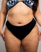 High-waisted black Brazilian bottoms showcased with a colorful flame-patterned bikini top, perfect for rave outfits.