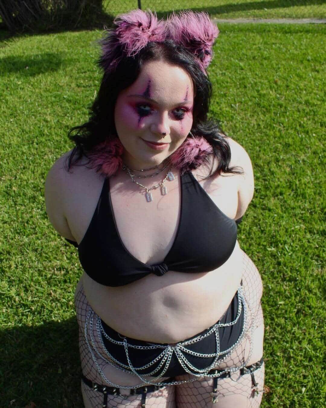 Model wearing a black bikini top and chain accessories, styled for a rave outfit in an outdoor setting.