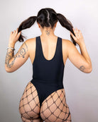 Model wearing a matte black sideboob bodysuit with fishnet stockings, showcasing a stylish back view for rave outfits.