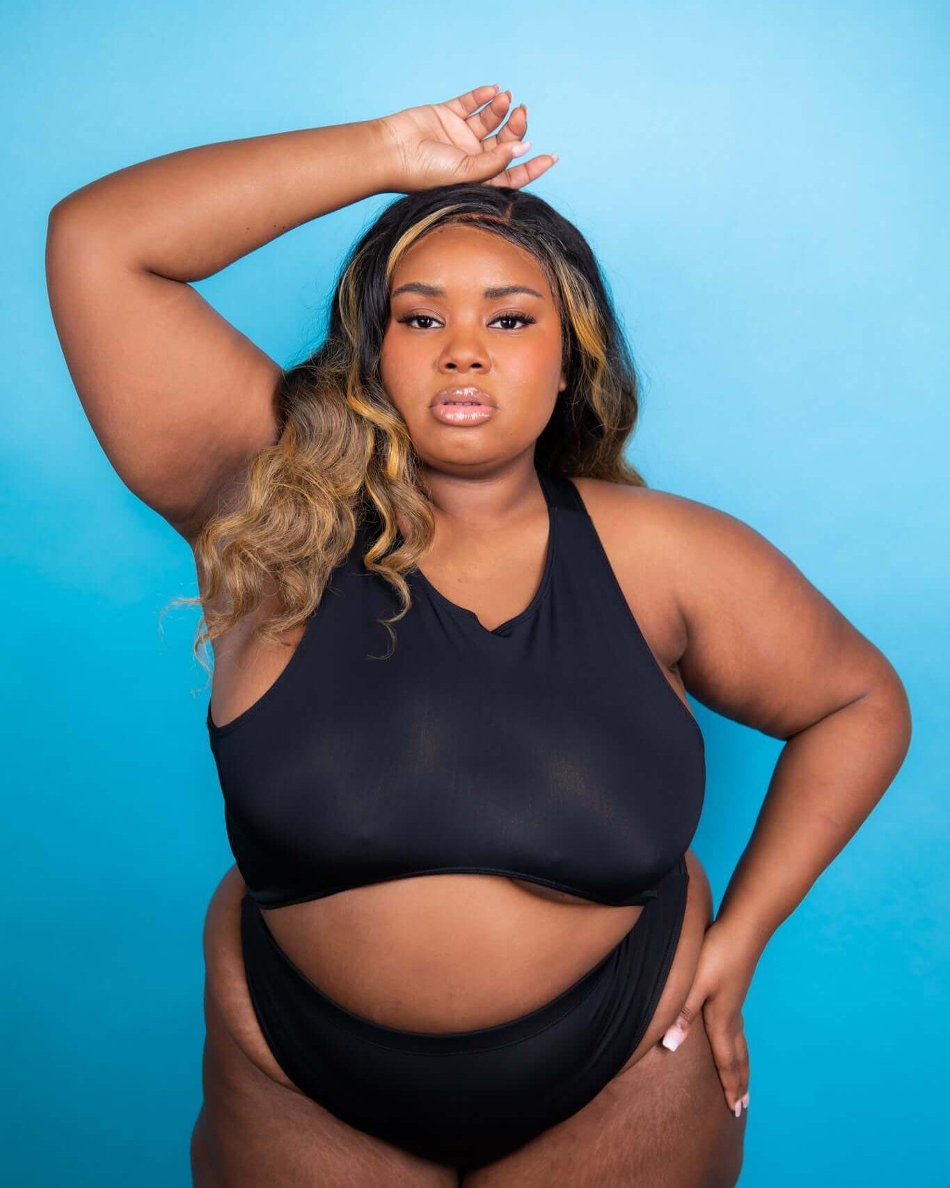 Woman modeling a matte black teaser top against a blue background, showcasing underboob style perfect for rave outfits.