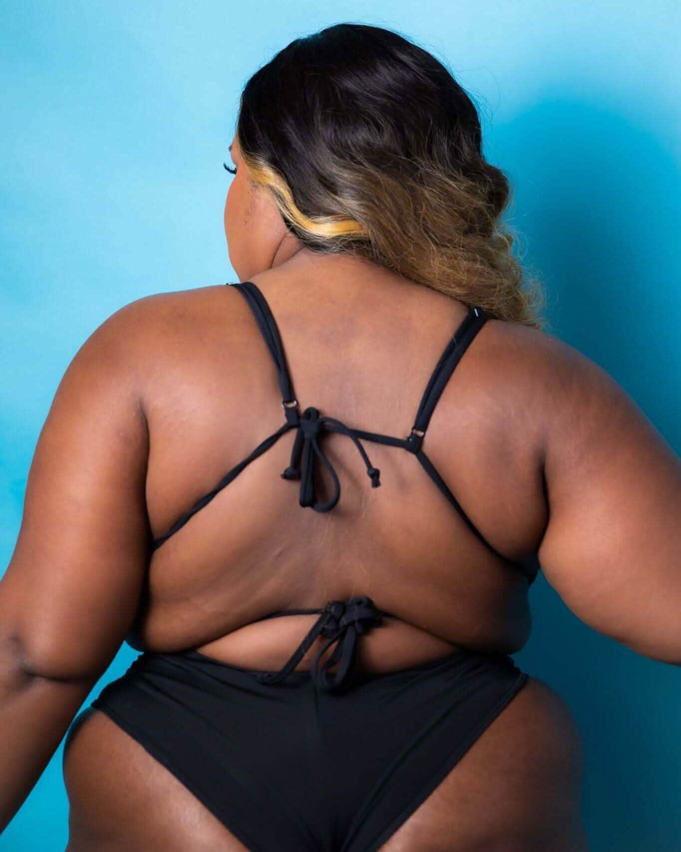 Back view of a model wearing a black tie-strap top, showcasing its adjustable fit and soft fabric. Perfect for rave outfits.