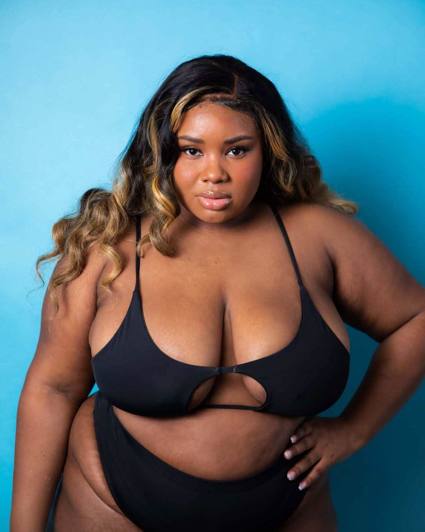 Plus-size model wearing a stylish black bikini set against a bright blue background, showcasing a confident pose.
