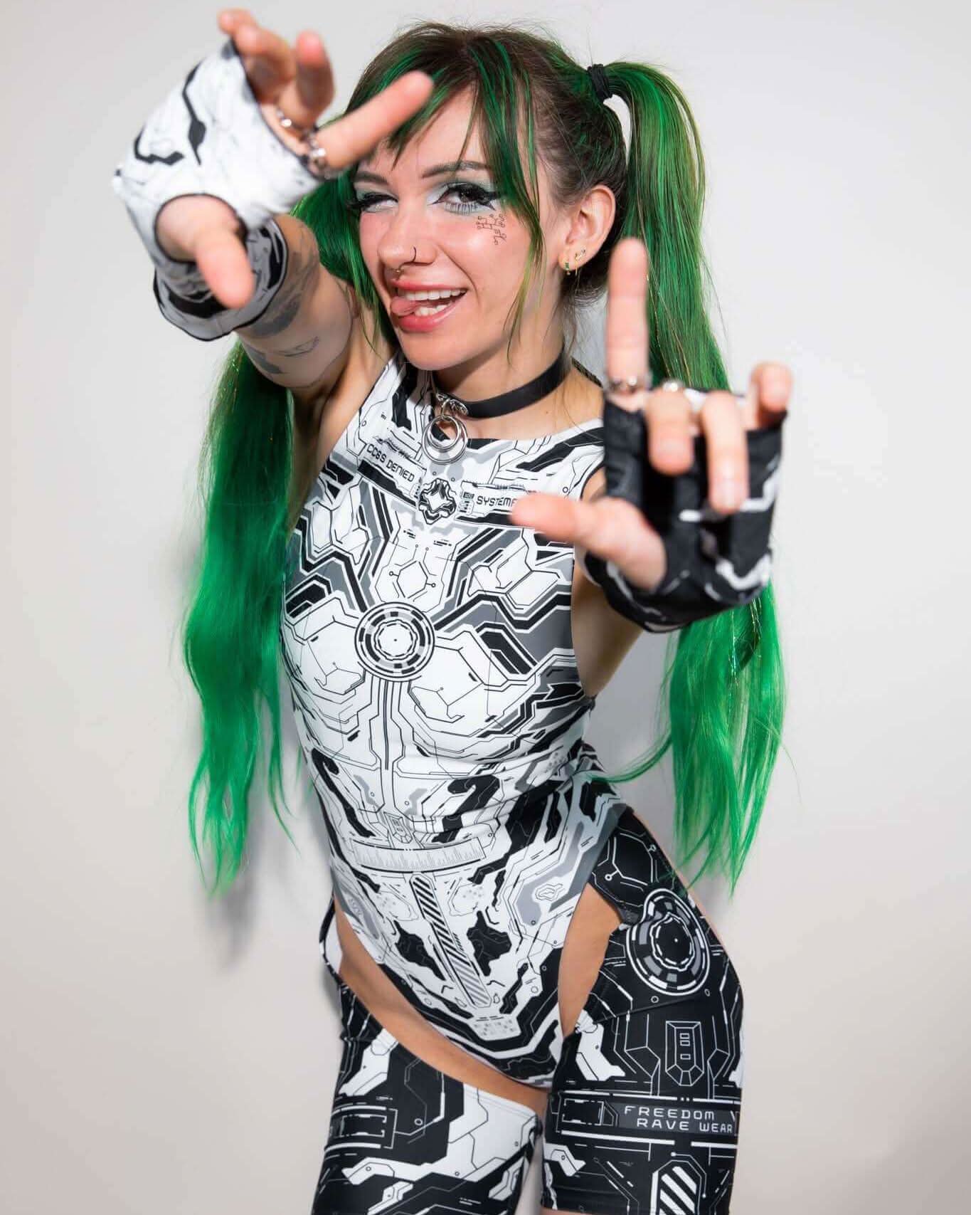 Rave outfit featuring a model in a futuristic black and white design with neon green hair, showcasing playful hand gestures.