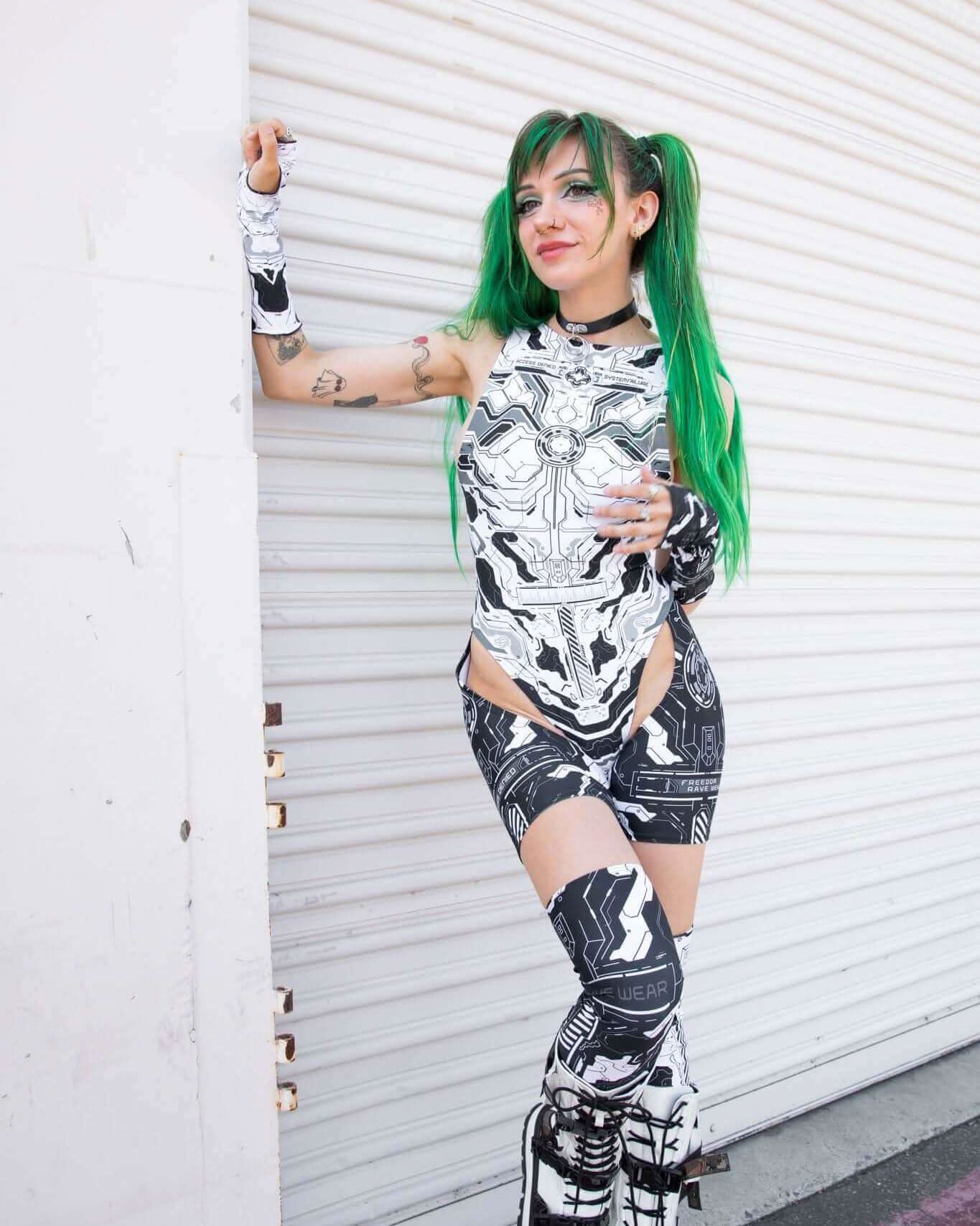 Woman in black and white robotic outfit with green hair, showcasing Mechanoid Leg Sleeves, perfect for festival rave outfits.