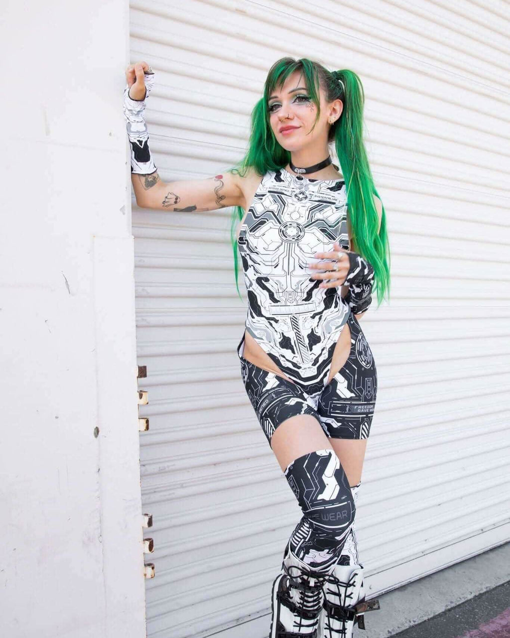 Woman in black and white robotic outfit with green hair, showcasing Mechanoid Leg Sleeves, perfect for festival rave outfits.