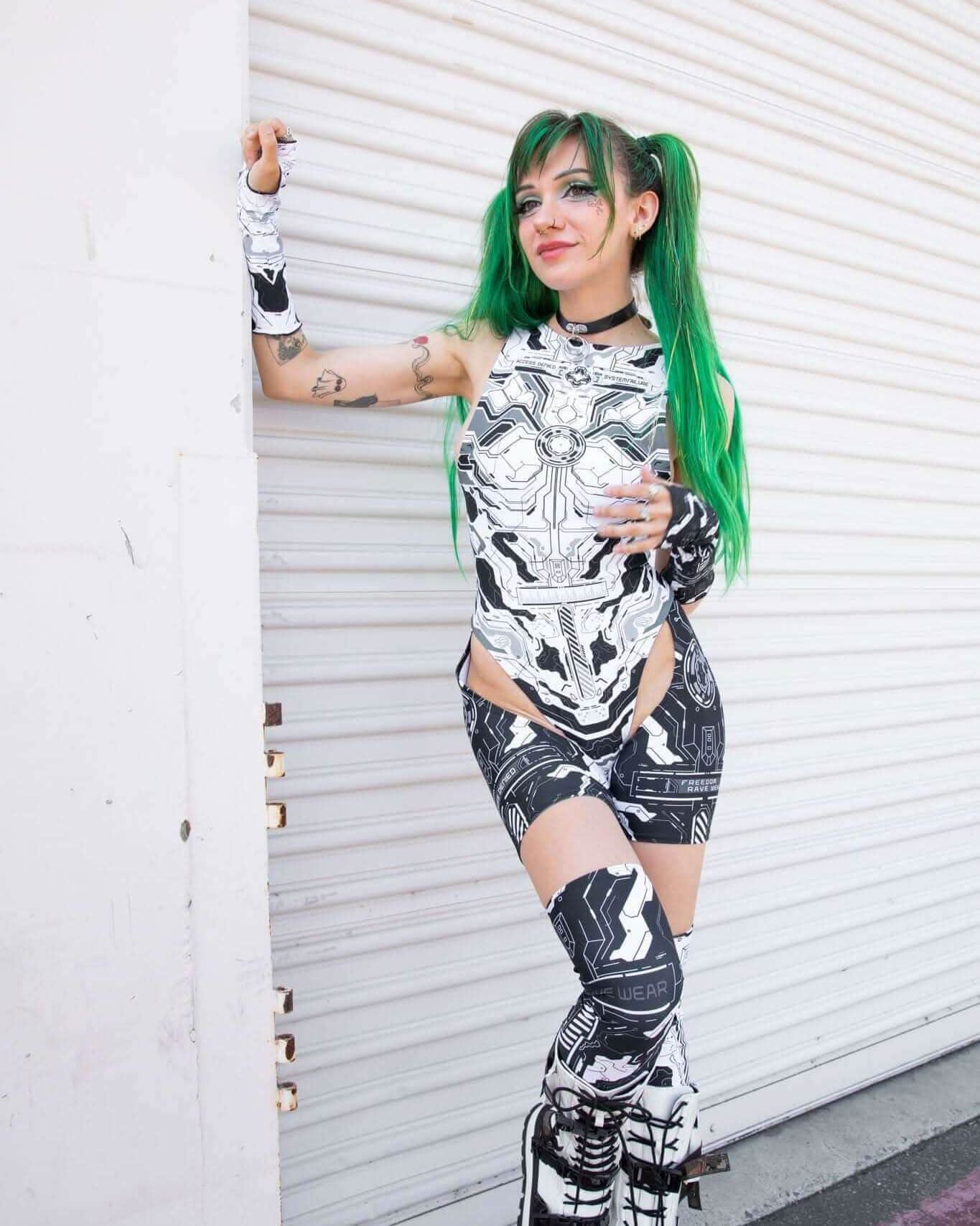 Woman in black and white robotic outfit with green hair, showcasing Mechanoid Leg Sleeves, perfect for festival rave outfits.