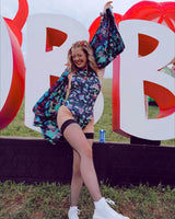 Young woman in a psychedelic mushroom bodysuit posing joyfully at a festival, showcasing vibrant rave outfit style.