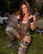 Festival model wearing black Charmer Chain harness over patterned rave bodysuit at outdoor rave venue