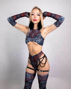 Model wearing dark floral rave bodysuit with chain harness details and thigh-high stockings in confident pose