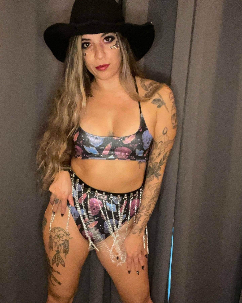 Tattooed model wearing Jail House print rave bodysuit with silver chain harness and black cowboy hat festival outfit