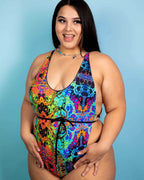 Curvy model wearing Lucidity rainbow psychedelic rave bodysuit with halter top and tie waist against blue background