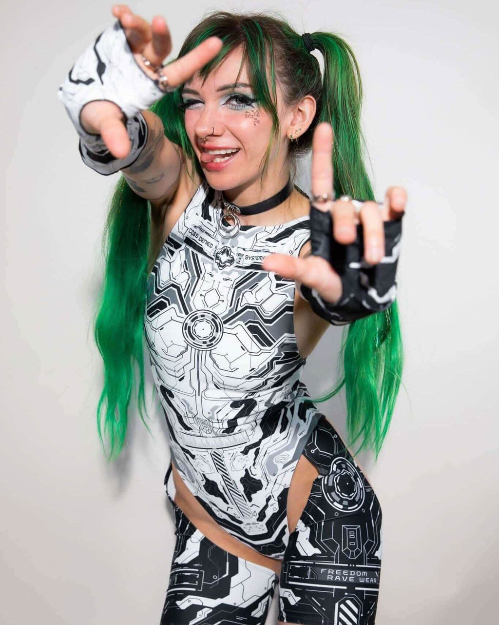 Woman in mechanoid rave bodysuit with circuit pattern posing dynamically at festival photoshoot with green pigtails