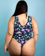 Back view of woman wearing black Mushies rave bodysuit with colorful psychedelic mushroom print against blue background