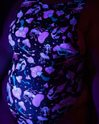 Rave bodysuit with glowing mushies pattern shown from side angle under blacklight revealing sideboob cutout design