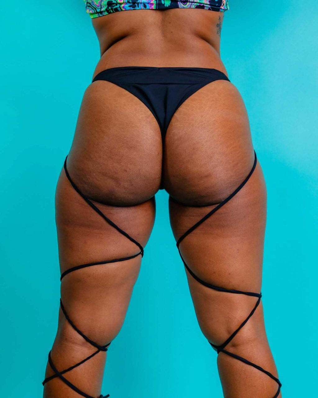 Back view of matte black strappy high hip rave pants with intricate leg wrapping details