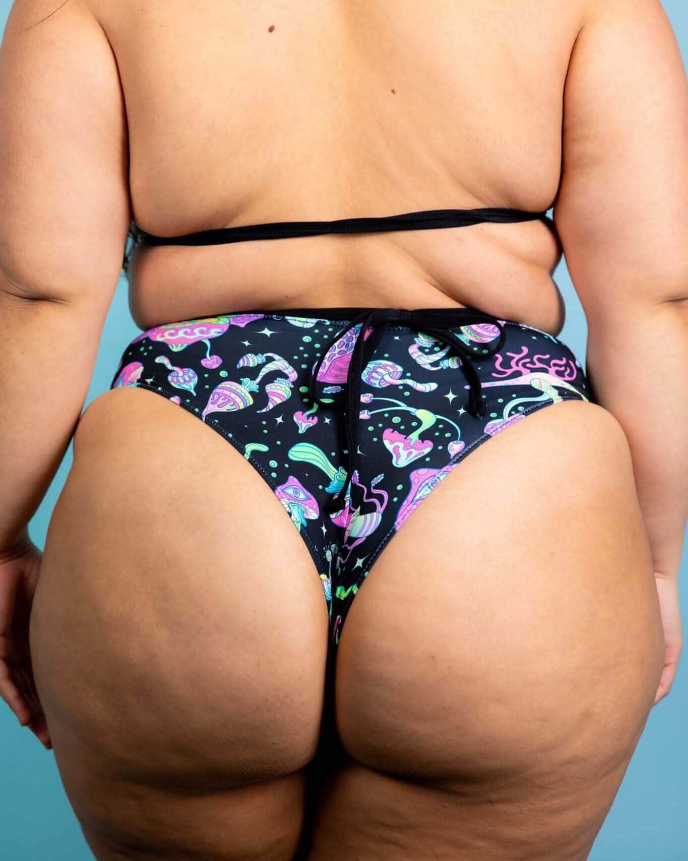 Back view of woman wearing Mushies high waisted rave pants with colorful mushroom print on black background