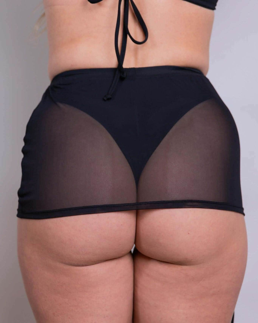 Back view of black mesh cinch rave skirt with adjustable drawstring worn by model against white background