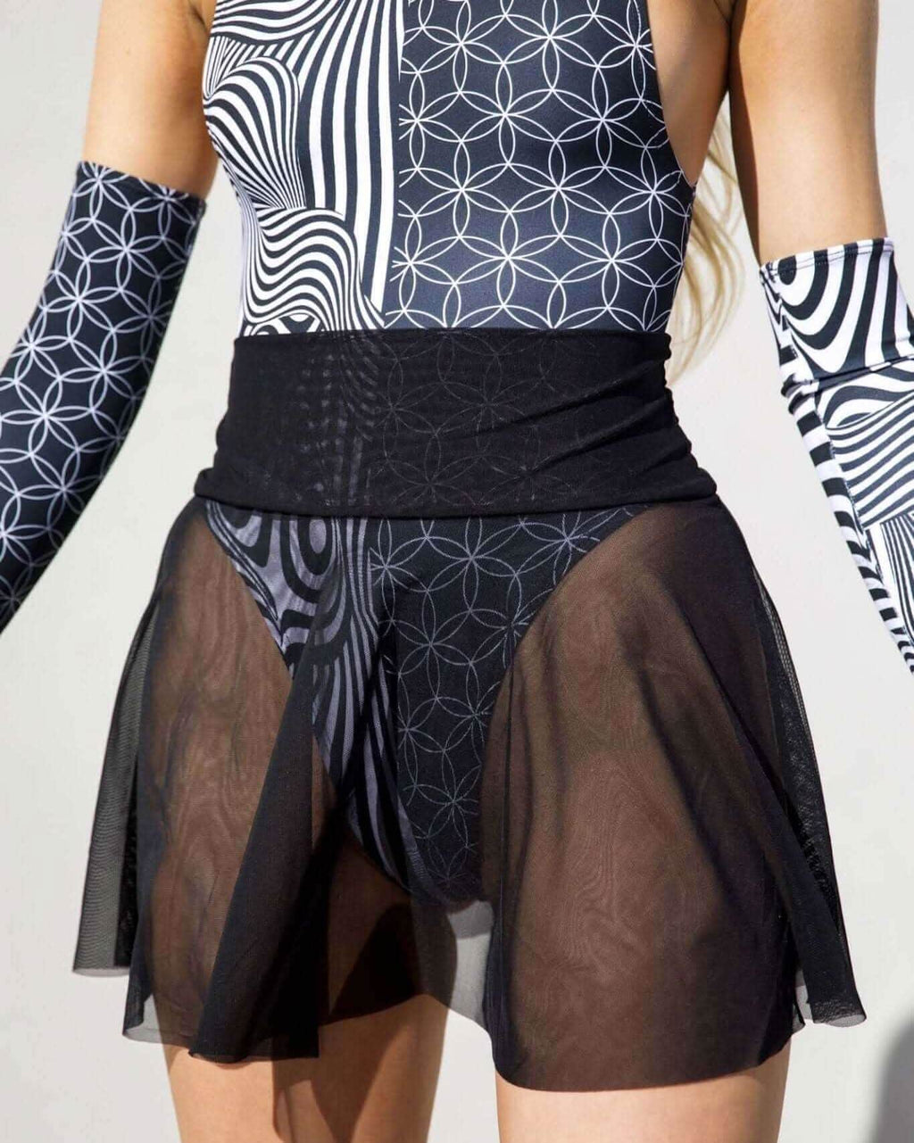 Black mesh rave skirt paired with geometric patterned bodysuit and matching arm sleeves for festival outfit styling