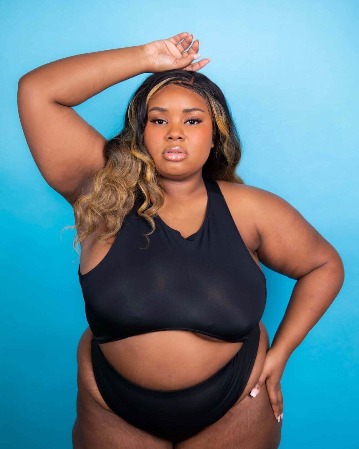 Plus-size model wearing matte black rave top two-piece set in confident pose against blue background