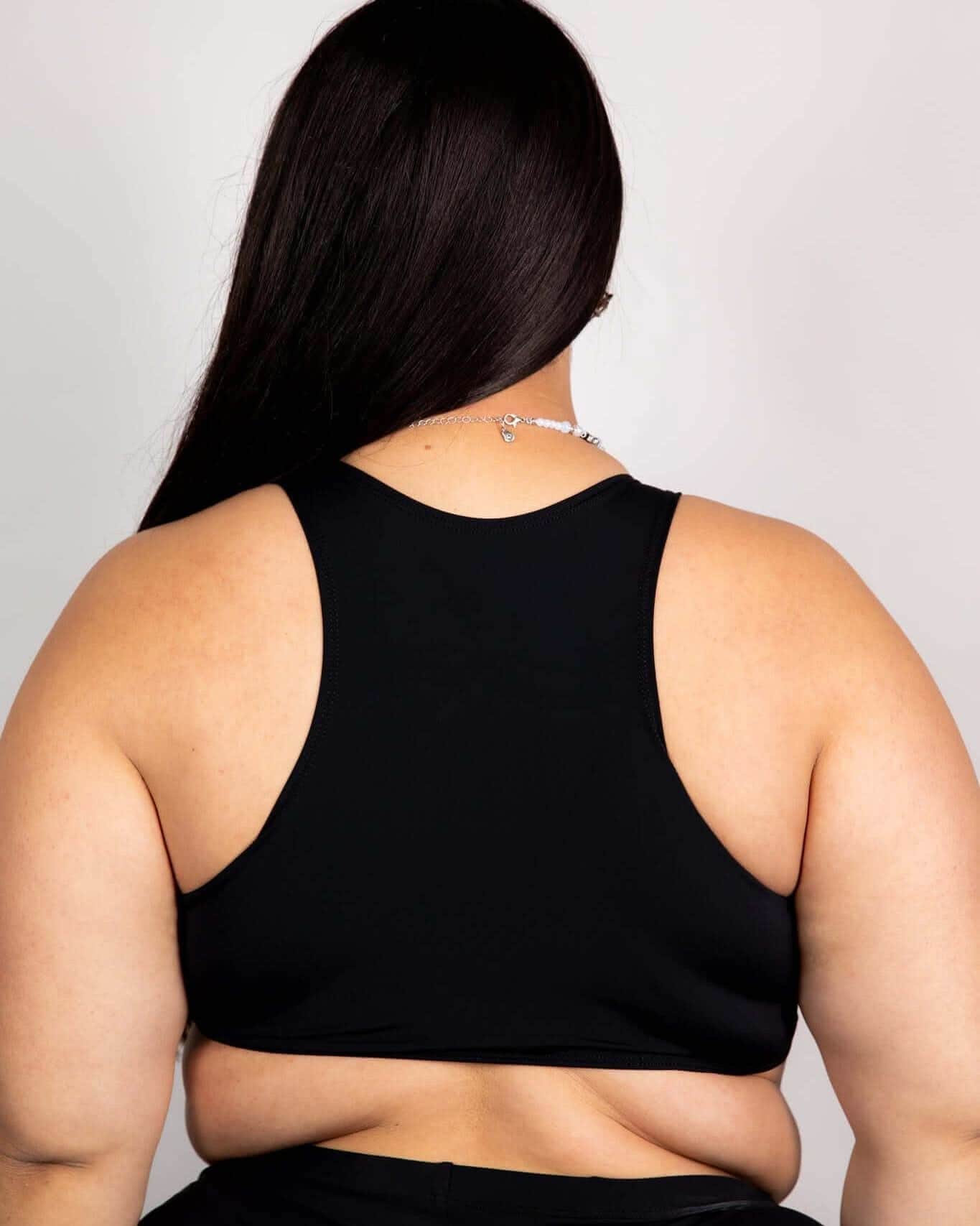 Back view of model wearing matte black rave top with racerback design and curved underboob cut