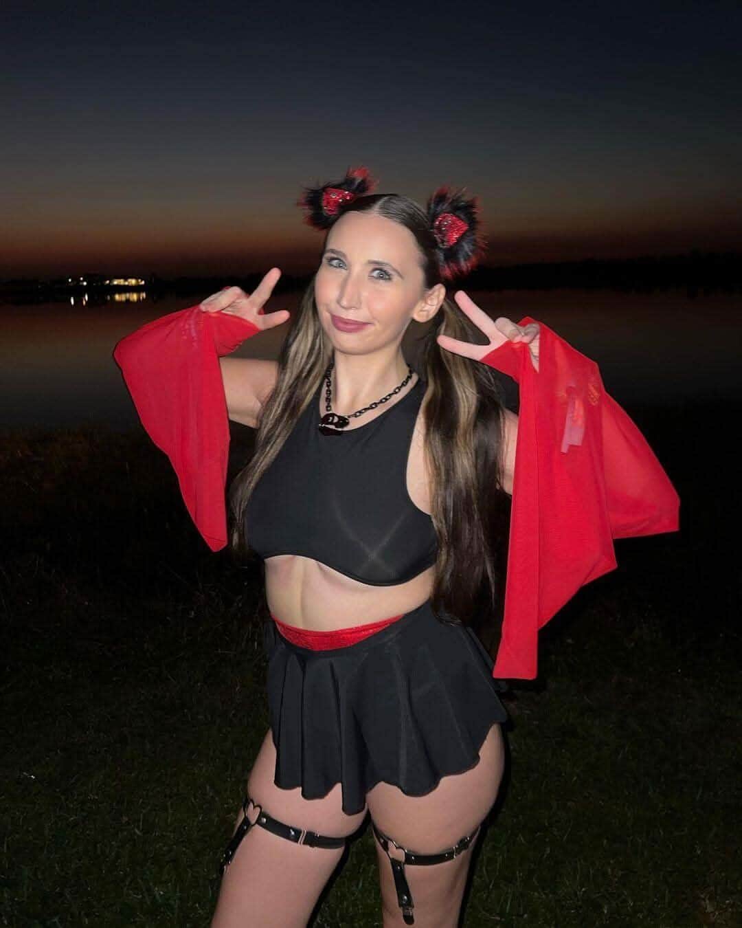 Woman wearing matte black rave top with red cardigan making peace signs in festival field setting