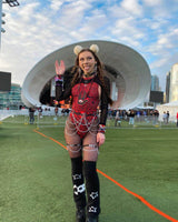 Woman in a red sideboob bodysuit with chains at a festival, showcasing stylish rave outfits against a modern backdrop.
