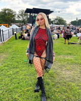 Young woman in a red sideboob bodysuit with fishnet tights at a festival, showcasing rave outfits and stylish festival fashion.