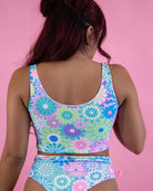 Model showcasing a pastel groovy flower print bikini top and bottom against a pink background, perfect for rave outfits.