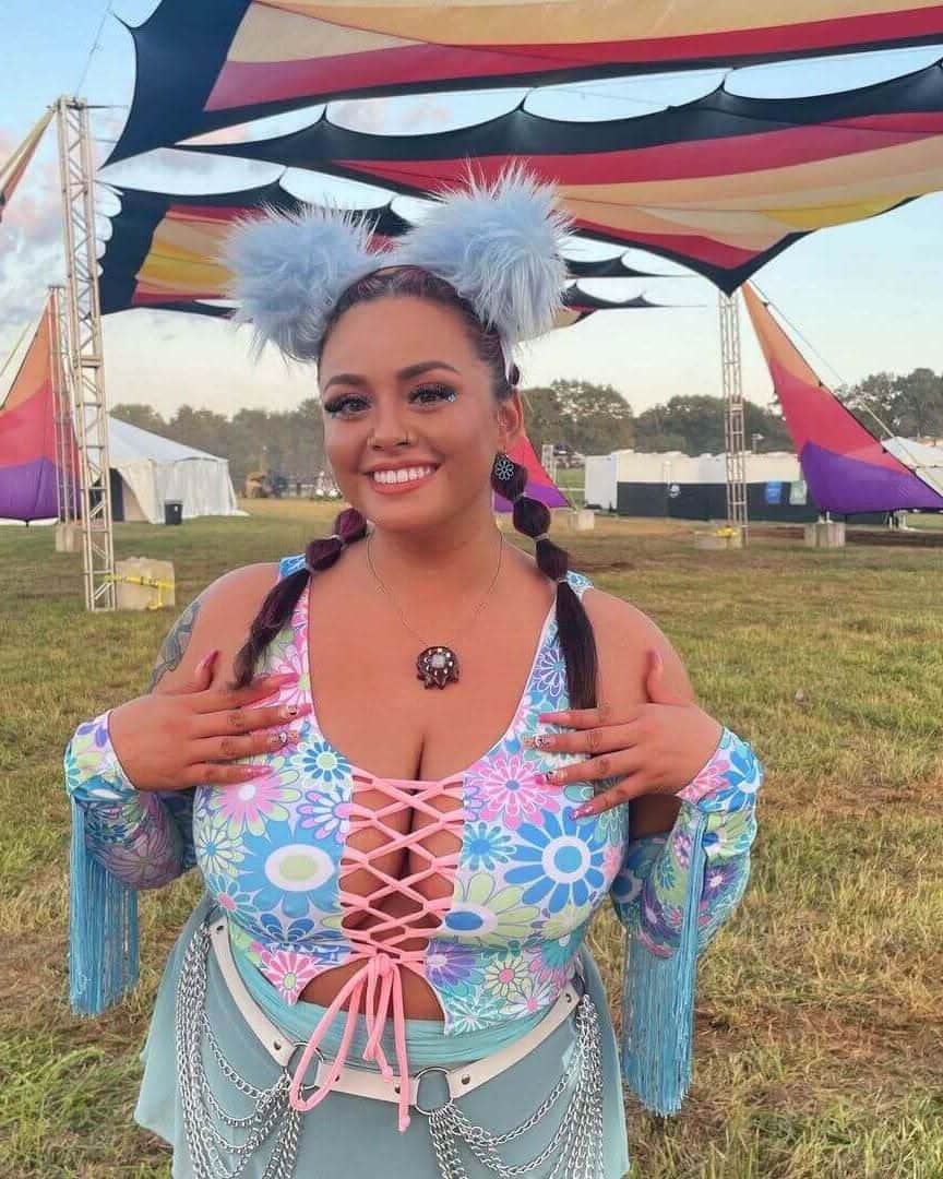 Woman in a pastel groovy flower print lace-up top at a festival, styled for rave outfits in a vibrant outdoor setting.