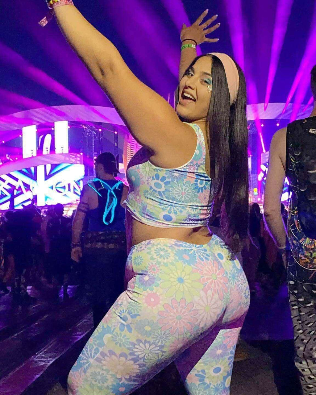 Woman wearing pastel groovy flower print lace-up tank top at a vibrant rave, showcasing a fun festival atmosphere.