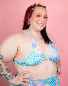 Model wearing vibrant pastel floral bikini top against pink backdrop, showcasing trendy rave outfits.