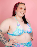 Model wearing vibrant pastel floral bikini top against pink backdrop, showcasing trendy rave outfits.