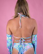 Woman wearing a pastel groovy flower print wrap bikini top with creative tying, showcasing a summer vibe against a pink background.
