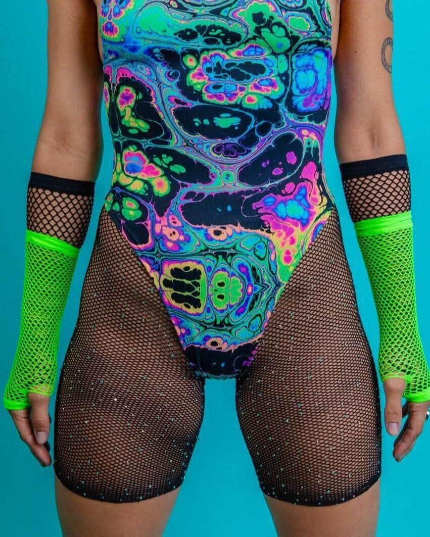 Colorful rave outfit featuring a vibrant bodysuit and black fishnet shorts with green arm warmers. Perfect for festival wear!