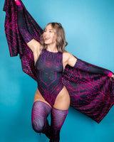 Woman in vibrant pink and black rave outfit with matching leg sleeves, posing against a blue backdrop.