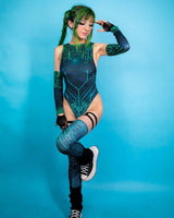 Model in teal rave outfit with circuit pattern, wearing leg sleeves and sneakers against a blue background.
