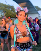 Woman wearing colorful rave outfit with chain belt and accessories at a festival, surrounded by festival-goers.