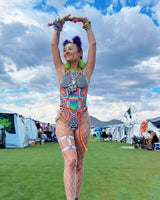 Model in a colorful Technicolor Sideboob Bodysuit, posing at a vibrant outdoor festival with tents in the background.