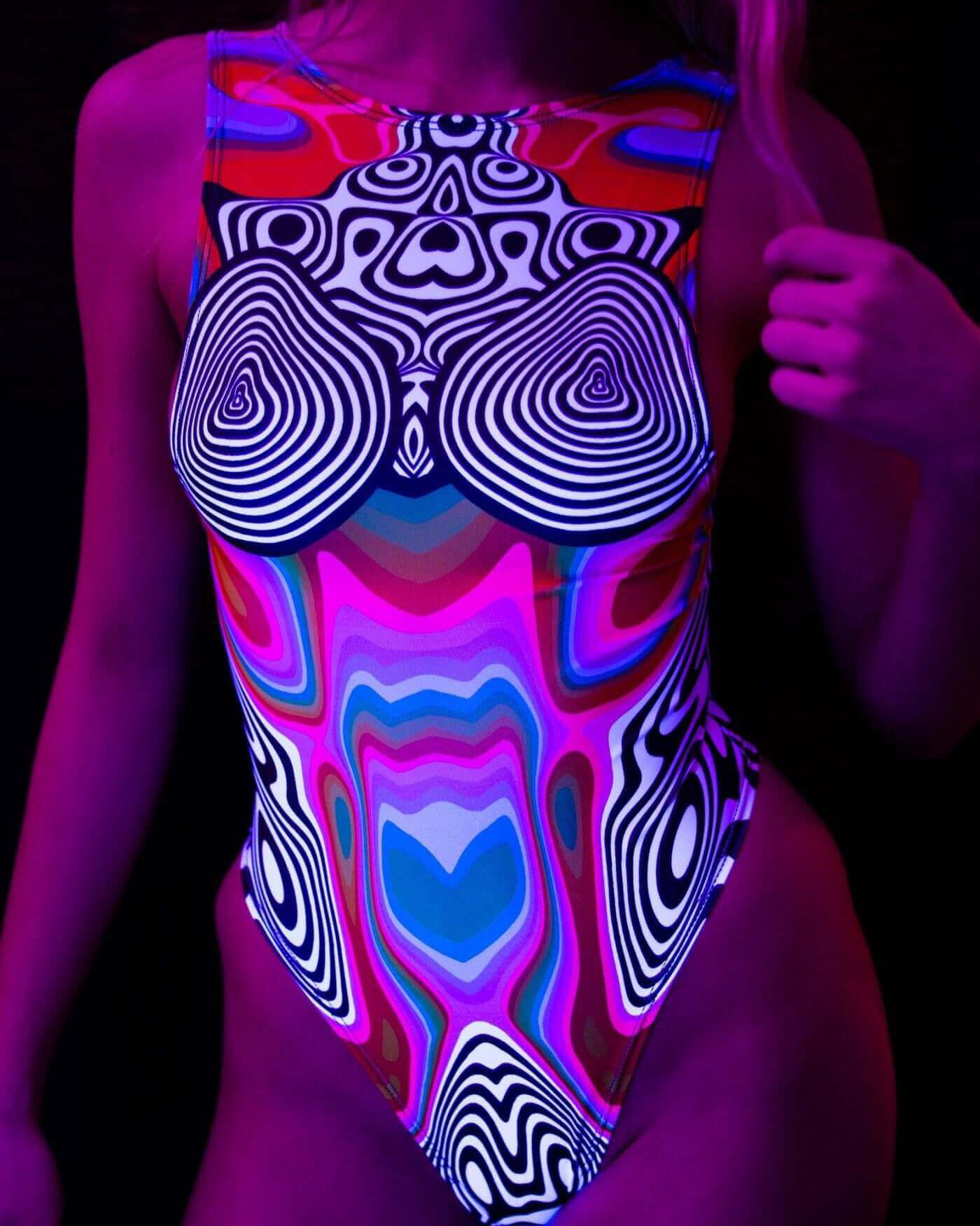 Model wearing a Technicolor sideboob bodysuit with psychedelic rainbow print, showcasing the vibrant design in blacklight.