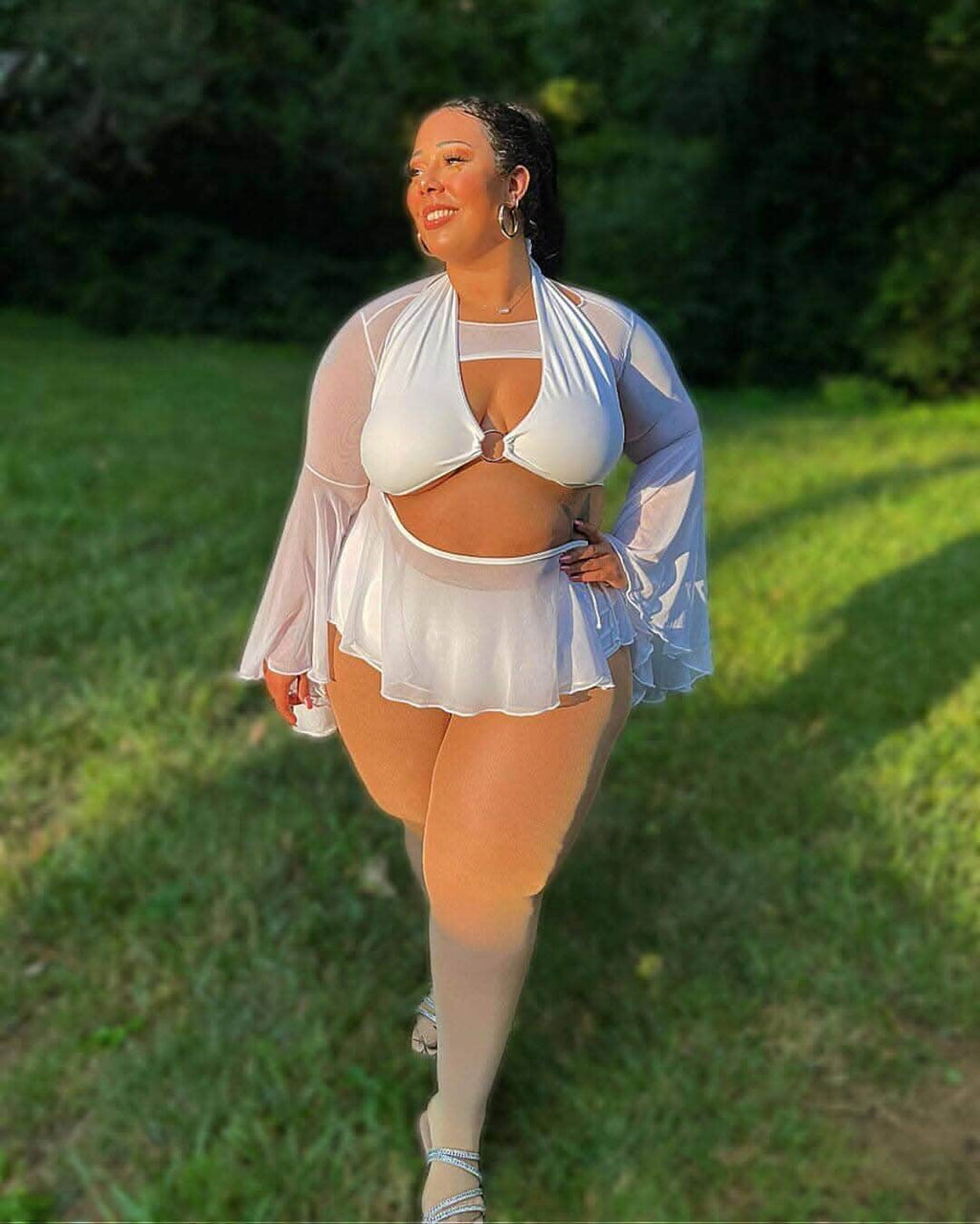 Model showcasing a White Eco-Luxe O-Ring Halter Top in a lush green setting, ideal for summer rave outfits.